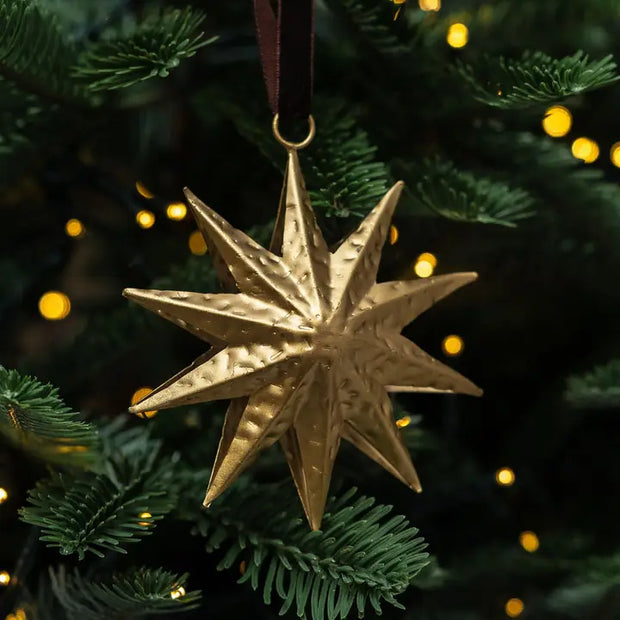 Gold star-shaped Christmas ornament on a tree with blurred lights in the background