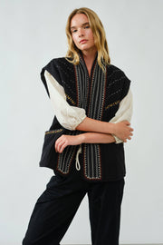 Woman wearing a black and white embroidered jacket against a plain background
