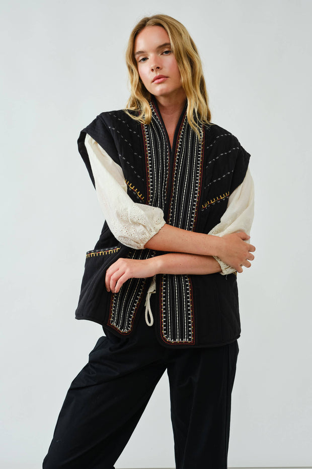 Woman wearing a black and white embroidered jacket against a plain background