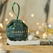 Rose Petal Bath Bombs Christmas Bauble -Bramley product packaging on a wooden stand with blurred lights in the background