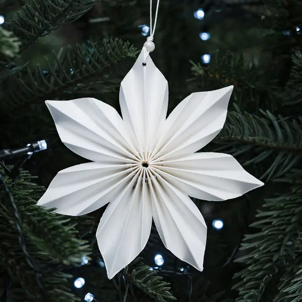 White paper star ornament hanging on a Christmas tree.