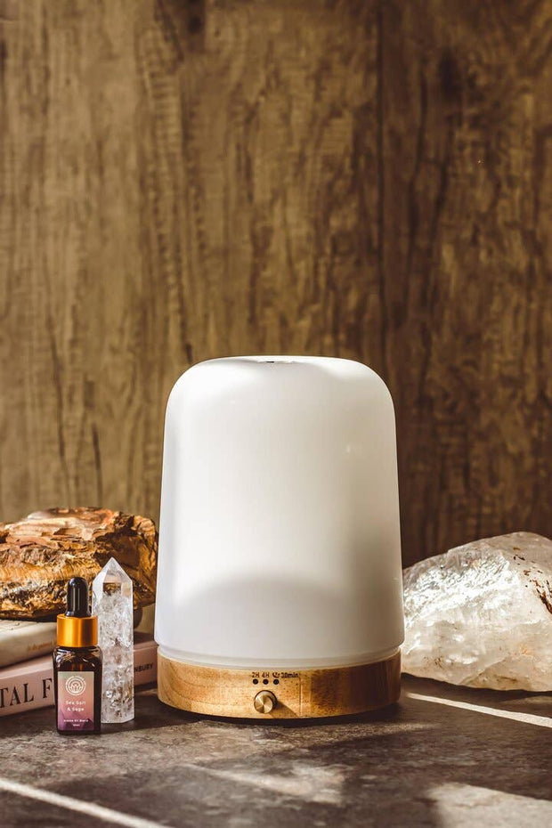 White diffuser with bamboo  base on a wooden surface with crystals and a book in the background