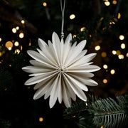 White paper star ornament hanging on a Christmas tree with blurred lights in the background