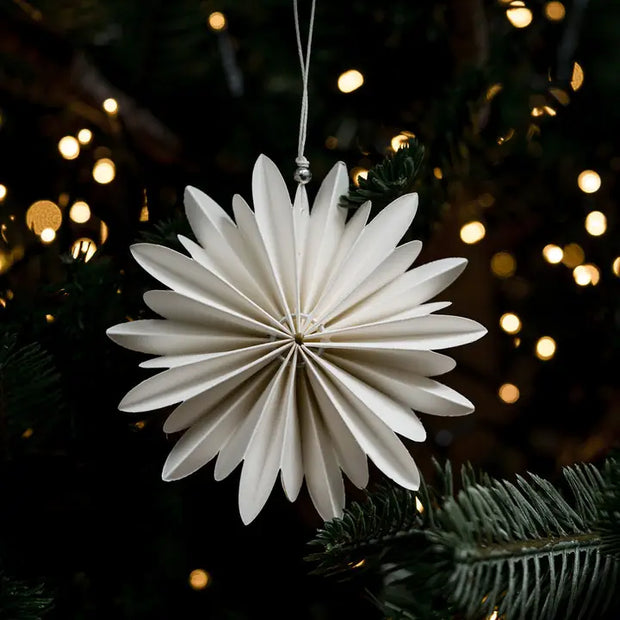 White paper star ornament hanging on a Christmas tree with blurred lights in the background