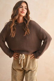Woman wearing a brown knitted sweater and beige pants against a beige background, Miou Muse