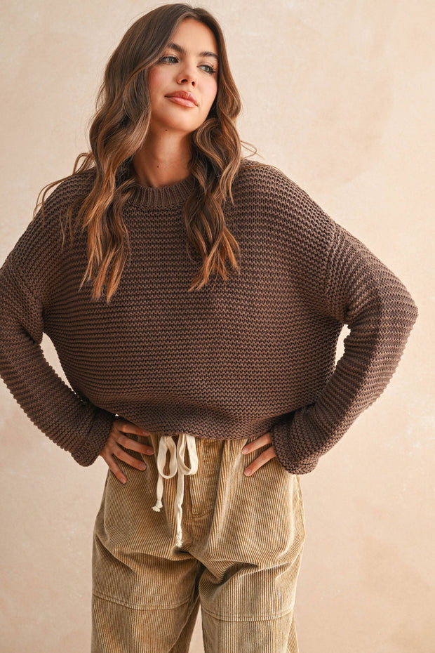 Woman wearing a brown knitted sweater and beige pants against a beige background, Miou Muse