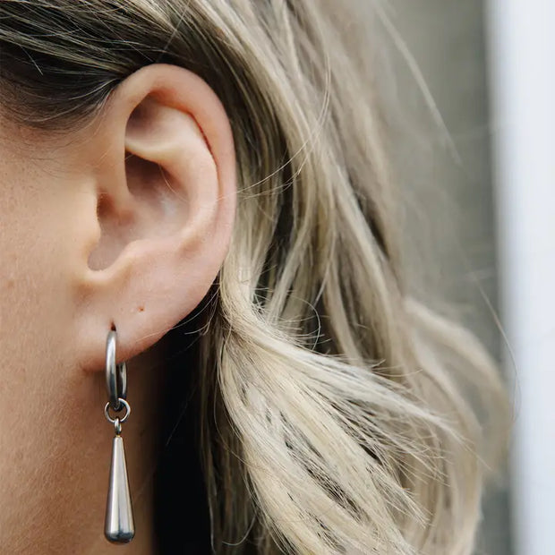 Close-up of an ear wearing a silver hoop earring with a dangling teardrop charm.