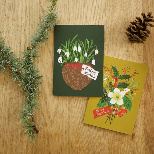 Two Christmas-themed greeting cards on a wooden surface with decorative elements.