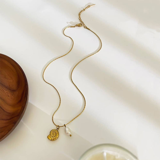Gold necklace with a spiral shell pendant and pearl on a light background