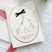 Christmas card with mistletoe design and 'Christmas Kisses' text on a white background.