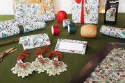 Christmas gift wrapping materials including wrapped presents, ribbons, and decorative tags on a green table.