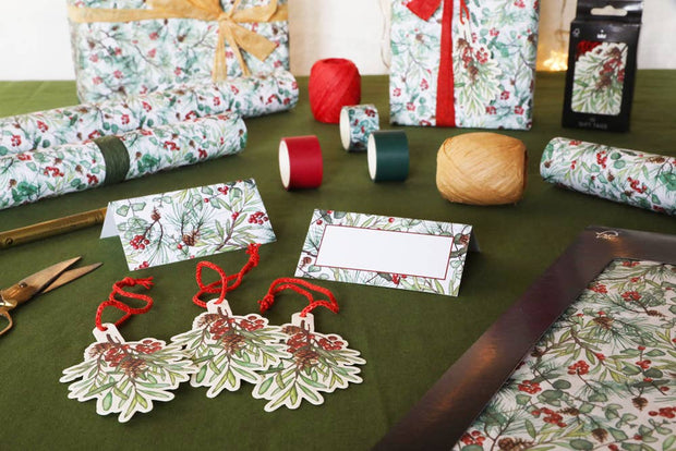 Christmas gift wrapping materials including wrapped presents, ribbons, and decorative tags on a green table.