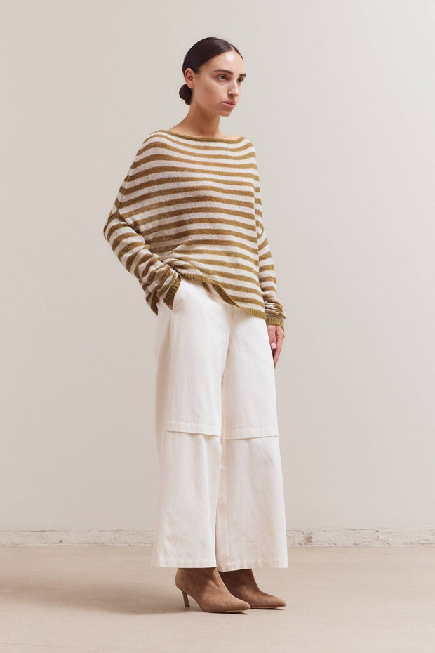 Woman wearing a striped sweater and white pants against a plain background