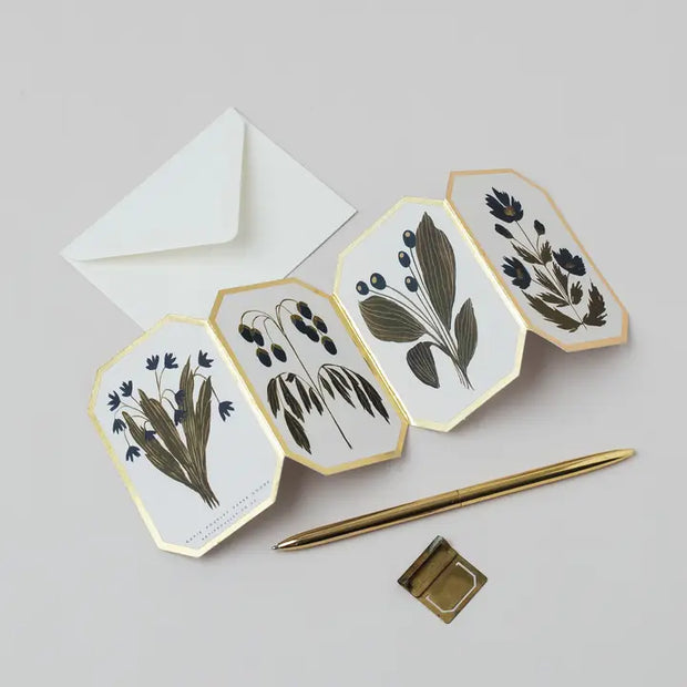 Hexagonal concertina card with floral designs, a white envelope, and a gold pen on a light gray background