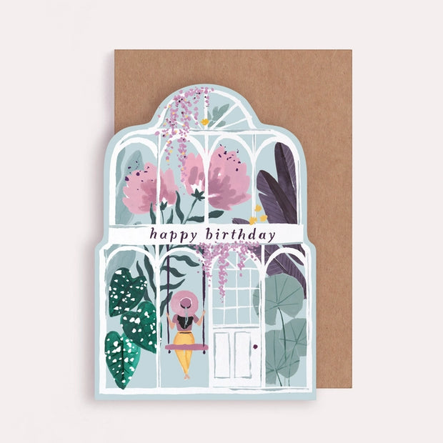 Giant peonies and lush green foliage are blooming on this greenhouse birthday card, featuring a relaxed girl in a big spring hat sitting on a swing, with the caption ‘happy birthday’. 