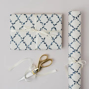 Gift wrapped in blue and white patterned paper with a gold scissors on a light gray background