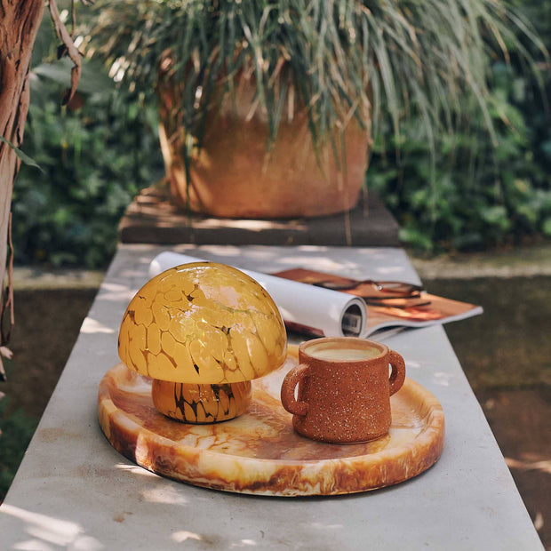 Decorative mushroom lamp and cup on a stone platter with a garden background