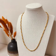 Gold necklace on a mannequin bust with a vase of dried plants in the background