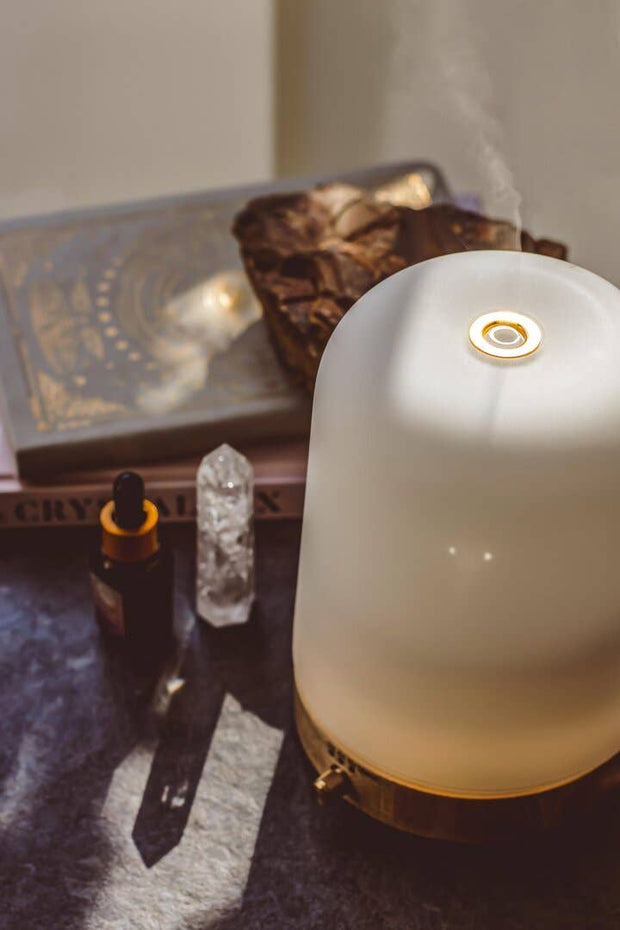 Aromatherapy diffuser emitting steam on a surface with books and crystals.