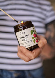 Person holding a lit Aery Tomato Leaf candle with a striped shirt in the background