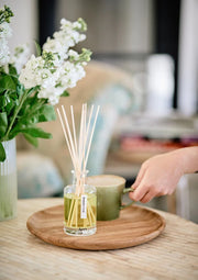 Tomato Leaf Reed Diffuser with reeds on a wooden tray next to a vase of flowers in a home setting