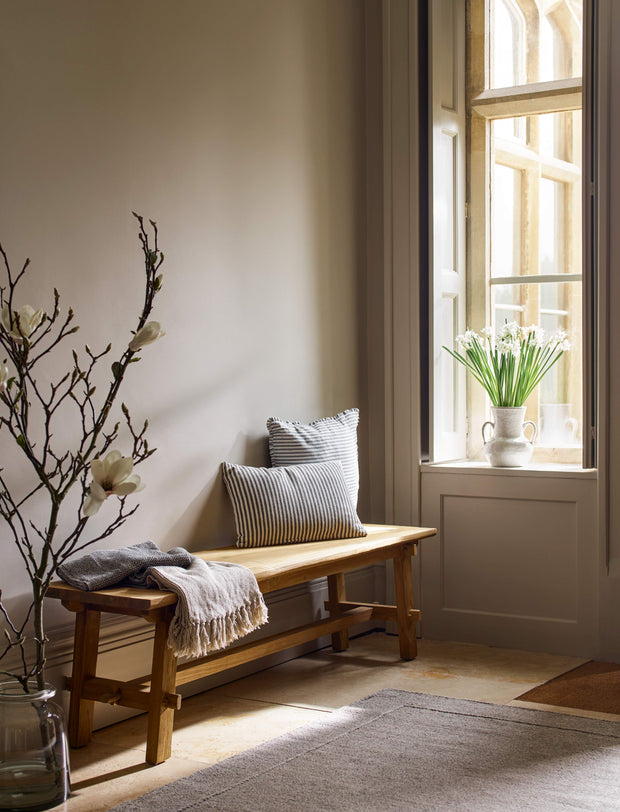 Nestled corner of a room with a wooden bench, pillows, and a large window.