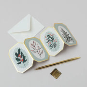 Hexagonal fold out cards with christmas loral designs on a light gray background with a pen and envelope.
