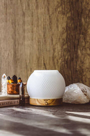 White diffuser with wooden base on a surface with crystals and books in the background