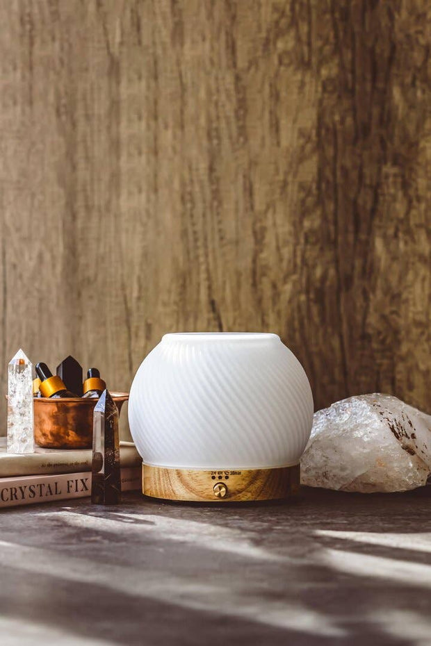 White diffuser with wooden base on a surface with crystals and books in the background
