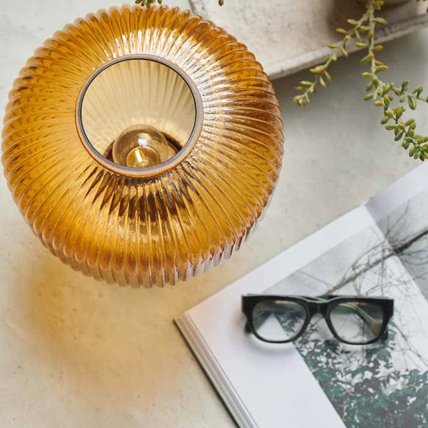 Round amber glass led lamp on a surface with a book and glasses nearby