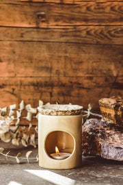 Ceramic oil burner with a lit candle on a wooden surface with a rustic background