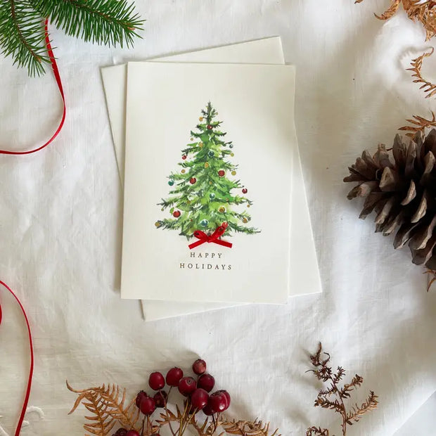 Christmas card with a decorated tree and 'Happy Holidays' text, surrounded by festive decorations on a white surface.