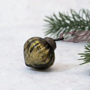 Decorative green ornament with ribbed texture on a white surface with a branch in the background