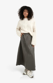 Woman wearing a cream sweater and gray skirt on a white background