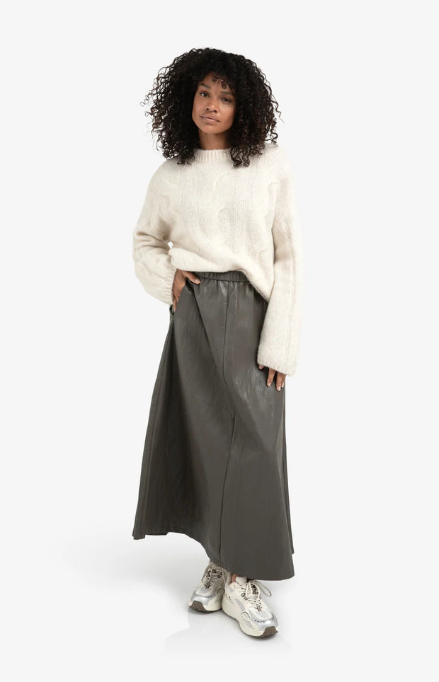 Woman wearing a cream sweater and gray skirt on a white background