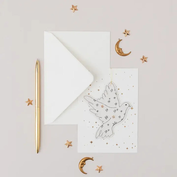 Decorative card with a dove illustration, gold pen, and small decorative items on a light gray background