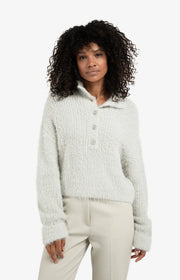 Woman wearing a light gray textured sweater and beige pants on a white background
