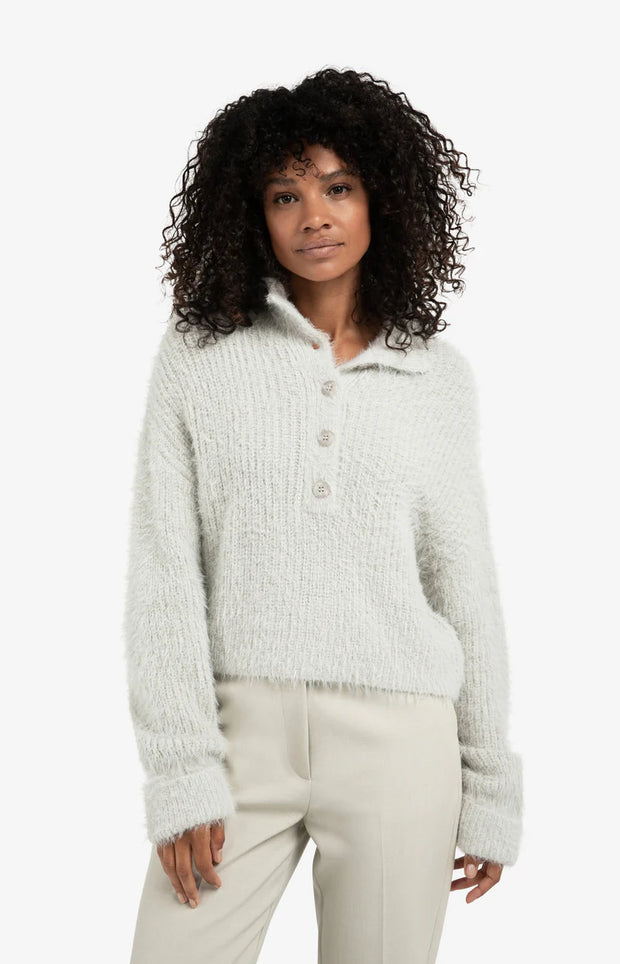 Woman wearing a light gray textured sweater and beige pants on a white background
