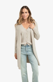 Woman wearing a grey cardigan, gilet, and light blue jeans on a white background