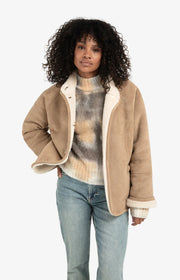 Woman wearing a beige jacket with a white shirt and blue jeans on a white background